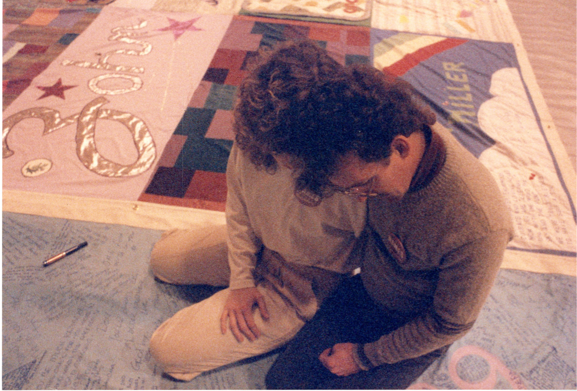 Two people console each other while viewing AIDS quilt.
